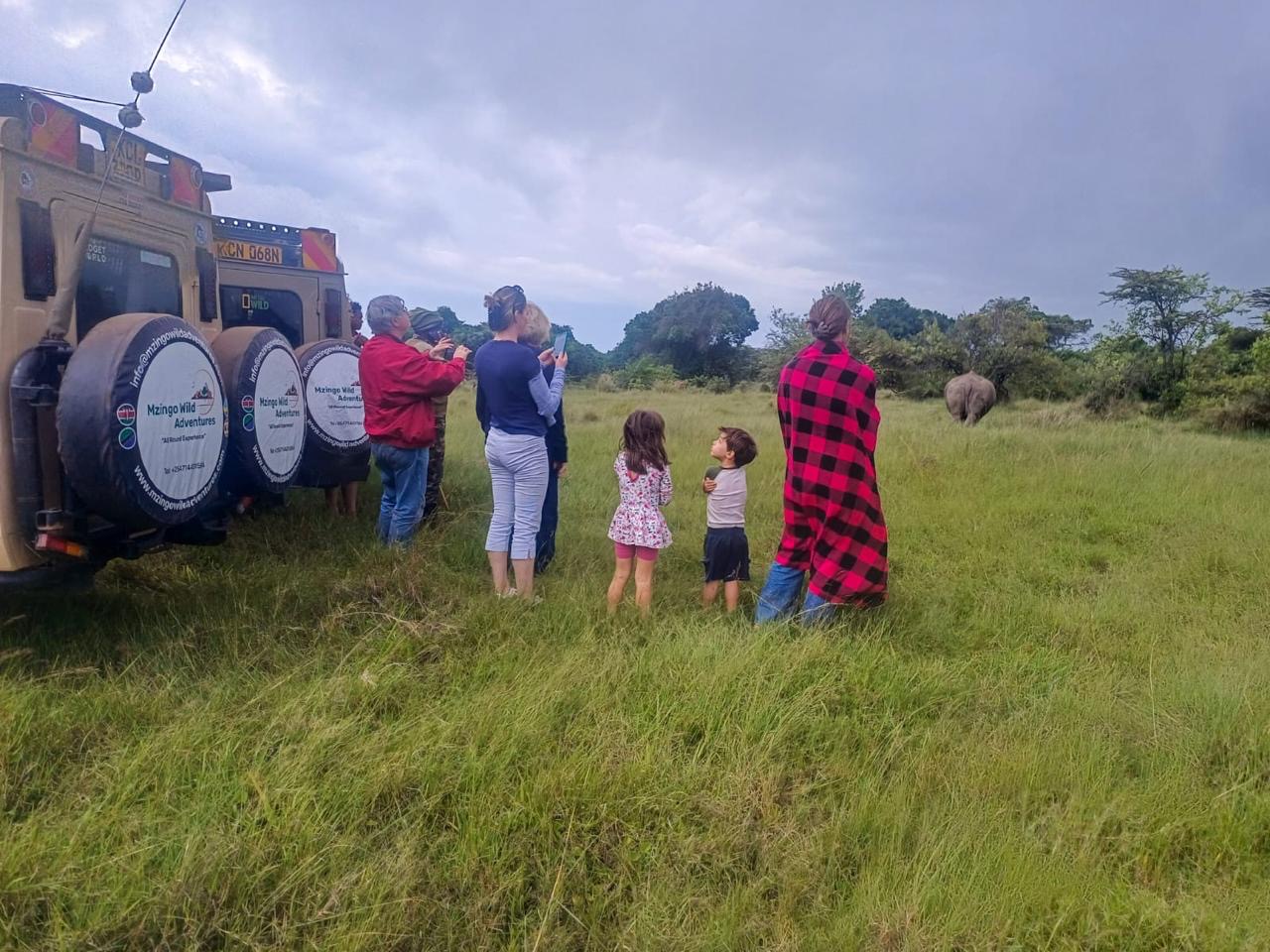 A family and their guide watching an elephant on the plains beside a Mzingo safari vehicle